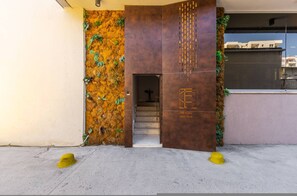 Ein Gebäudeeingang mit einer strukturierten Wand, einer Treppe und einer Tür mit einem Logo.