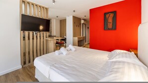Quarto de hotel com cama, escrivaninha, televisão e uma parede com detalhe em vermelho.