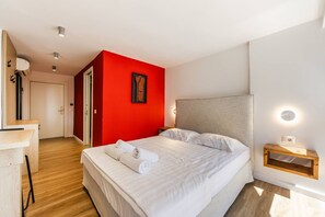 Habitació d'hotel amb un llit, una tauleta de nit, una paret decorativa vermella i un paviment de fusta.