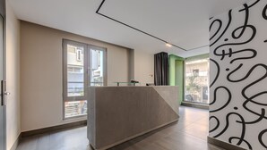 Um lobby moderno de hotel com uma mesa de recepção, janelas amplas e uma parede verde decorativa.