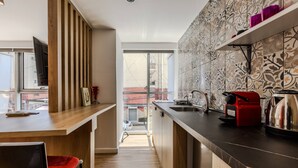 Uma cozinha moderna com balcão de madeira, uma cafeteira vermelha e vista para o exterior através de uma porta deslizante.