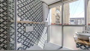 Un bagno moderno con un motivo a rilievo di piastrelle geometriche, cabina doccia in vetro e una grande finestra vista sulla città.