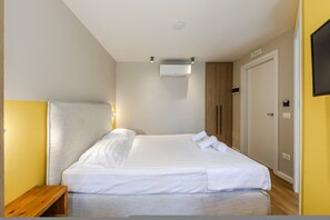 A hotel room with a bed, bedside table, and a mounted air conditioning unit. - Yellow Studio 106 Love in Colours Collection (Durrës)