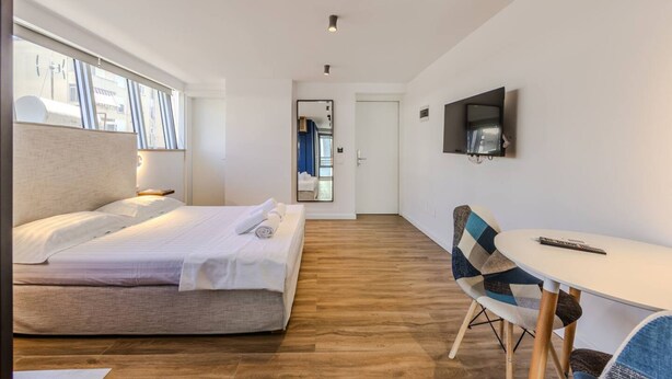 A hotel room with a bed, a desk, a chair, a television, and a door leading to another room. - Blue Studio 101 Love in Colours Collection (Durrës)