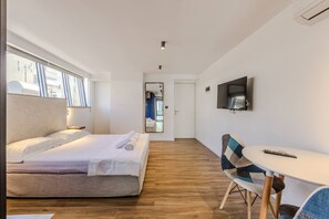 Habitació d'hotel amb un llit, escriptori, cadira, televisió i una porta que dona a una altra habitació.
