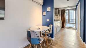 A modern kitchen with a white countertop, a built-in oven, and a window with curtains. - Blue Studio 101 Love in Colours Collection (Durrës)