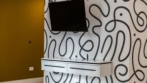 A wall-mounted TV on a white cabinet with a patterned wall in the background. - Honey Studio 115 Love in Colours Collection (Durrës)