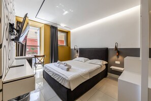 Quarto de hotel moderno com cama, escrivaninha, cadeira e uma janela ampla com cortinas.
