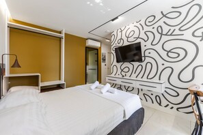 Quarto de hotel com cama, televisão na parede, roupeiro e secretária.