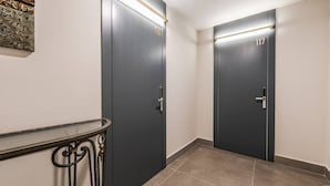 A hallway with two dark doors, each marked with a number, and a small table with a metal railing. - Golden Studio 117 Love in Colours Collection (Durrës)