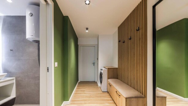 A hallway with a washing machine, a bench, and a door. - Green Apartment 103 Love in Colours Collection (Durrës)