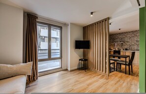 Ein modernes Wohnzimmer mit einer Couch, einem Fernseher, einem Essbereich mit Stühlen und einer Küche mit Arbeitsplatte und Schränken.
