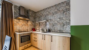 A kitchen with patterned backsplash, wooden cabinets, a stove, and a sink. - Green Apartment 103 Love in Colours Collection (Durrës)