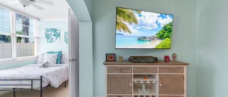 A bedroom with a bed, a TV mounted on the wall, and a wooden cabinet with drawers.