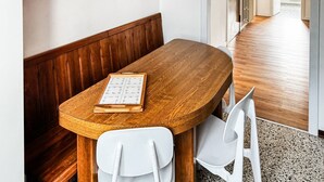 Une table en bois, une chaise blanche, un panneau rouge indiquant la présence d’une trousse de premiers secours et un tableau d’affichage avec une étagère en bois au-dessus.