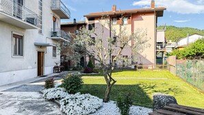 Un immeuble résidentiel doté d’un balcon, d’un petit jardin avec des fleurs blanches et d’un banc en bois.
