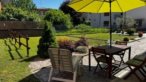 Une terrasse extérieure avec une table et des chaises, un parasol jaune et un petit coin jardin.