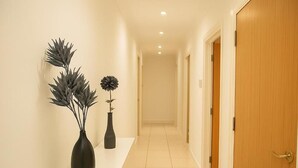 Un pasillo con una puerta de madera, una pared blanca y un suelo de baldosas.