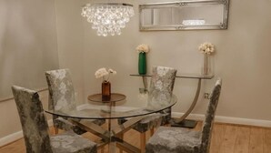 Comedor con mesa de vidrio, cuatro sillas, candelabro, espejo y dos jarrones con flores.