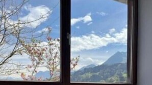 Habitació d'hotel amb una finestra gran, roba de llit a quadres i vista a les muntanyes i al cel.