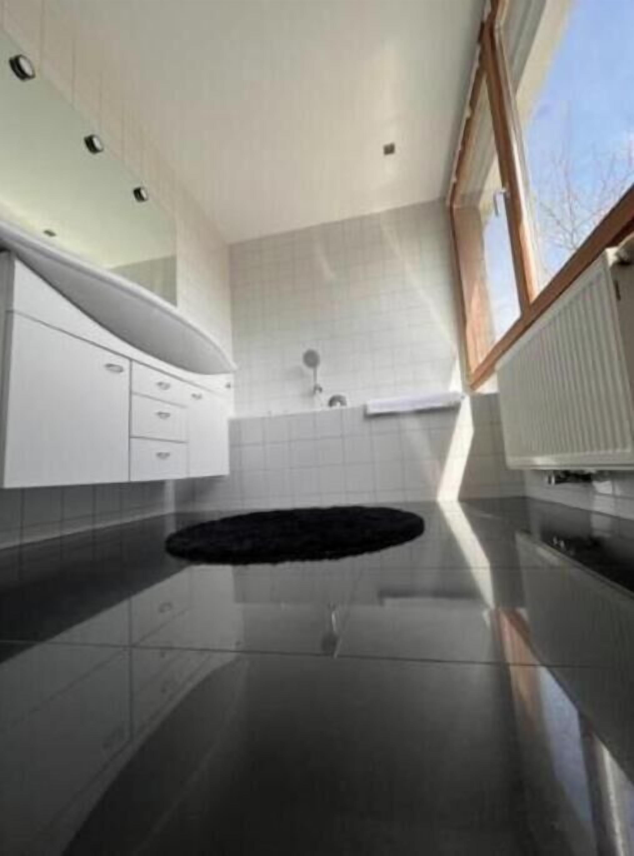 A modern bathroom with a black rug, white cabinets, and a window.