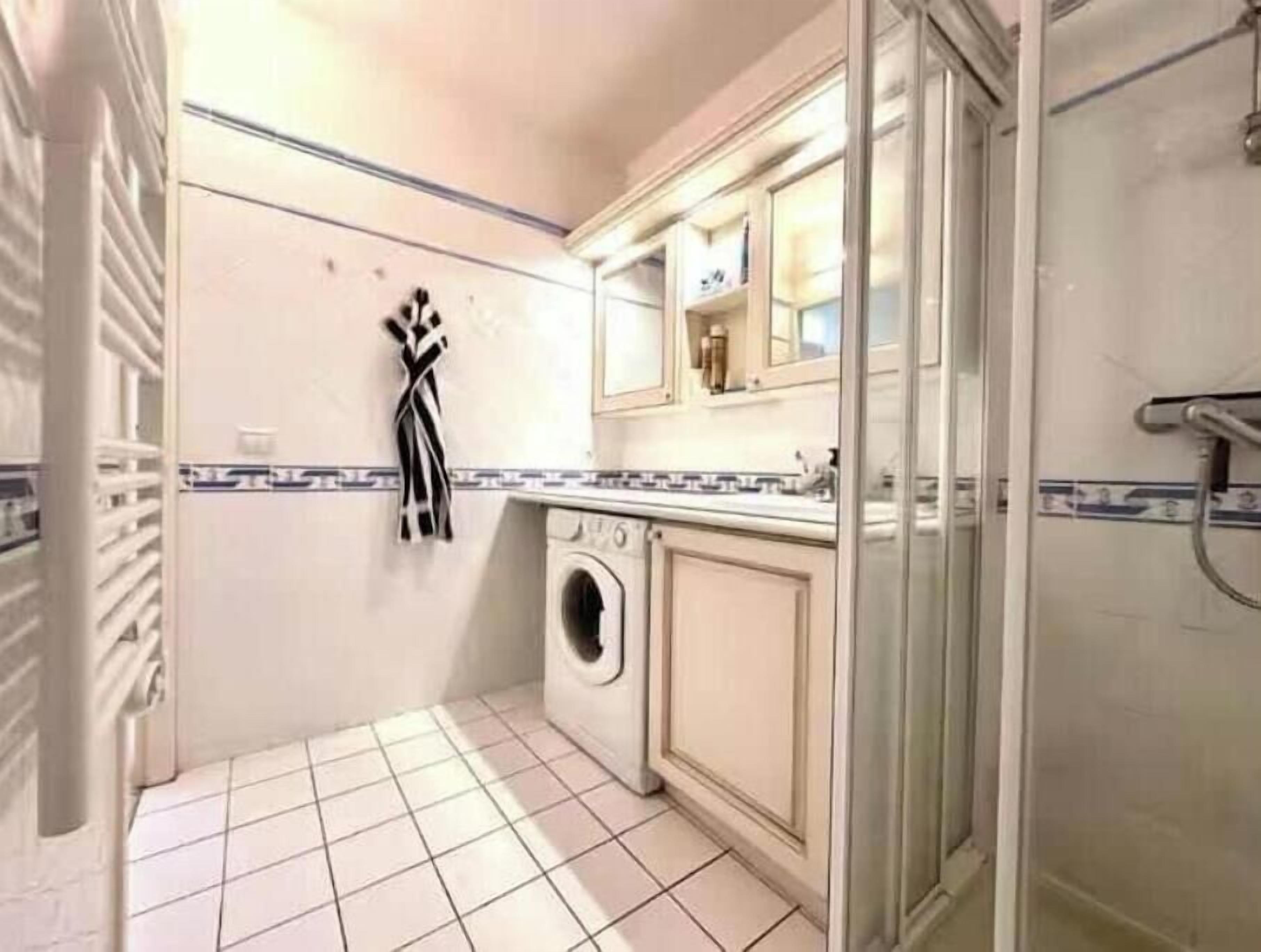 A compact bathroom with a washing machine, a towel rack, and a glass shower enclosure.