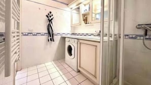 Un baño pequeño con lavadora, perchero para toallas y cabina de ducha de cristal.