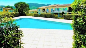 Una piscina con suelo de baldosas, rodeada de vegetación y edificios con balcones.