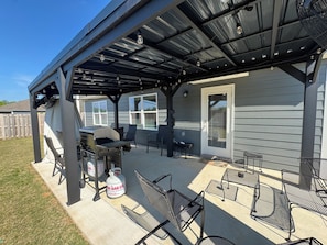 Eine überdachte Terrasse mit Grill, Sitzgelegenheiten im Freien und einer Gasflasche.