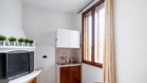 A compact kitchen with a built-in oven, a small cabinet, and a window with curtains. - GuestHost - San Vincenzo Apartment 1 Vigonza (Peraga)