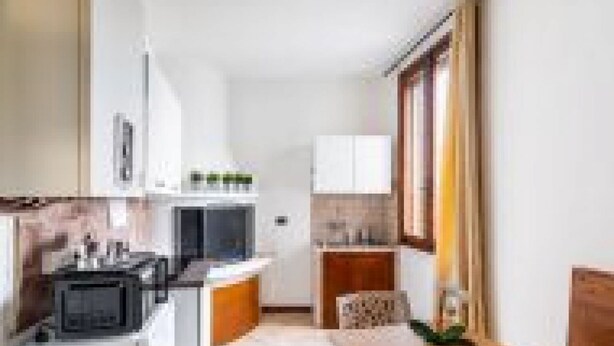 A compact kitchen with a microwave, stove, and cabinets, a small dining table with chairs, and a window providing natural light. - GuestHost - San Vincenzo Apartment 1 Vigonza (Peraga)