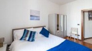 A bedroom with a bed, pillows, a wardrobe, and a chair. - GuestHost - San Vincenzo Apartment 1 Vigonza (Peraga)