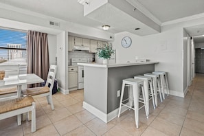 Eine moderne Küche mit weißen Schränken, einer zentralen Kochinsel, Barhocker und einem Essbereich mit Tisch und Stühlen.
