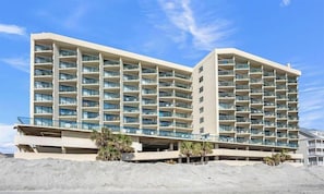 Ein mehrstöckiges Hotel mit Balkonen, einer Tiefgarage und Palmen.