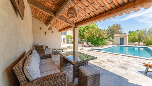 A covered outdoor seating area with wicker furniture, a pool, and a view of the surrounding landscape.