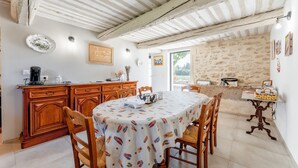 A dining area with a table covered in a patterned tablecloth, wooden chairs, a wooden cabinet, and a stone wall.