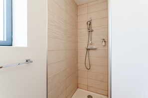 Une petite salle de douche carrelée, équipée d’un pommeau de douche à main et d’un robinet mural.