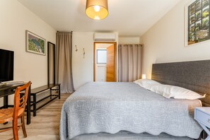 Ein Schlafzimmer mit Bett, Nachttisch, Schreibtisch, Stuhl und Blick ins Freie.