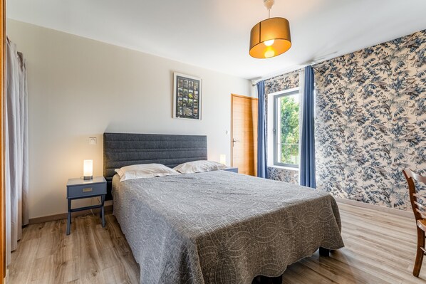 A bedroom with a bed, bedside table, lamp, and a window with curtains.
