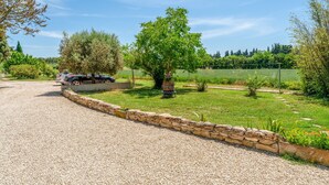 A gravel driveway leading to a parked car, a stone wall, and a well-maintained grassy area with trees and shrubs. - Bed and Breakfast 'Le Grenier' with Shared Pool, Wi-Fi and Air Conditioning (L'Isle-sur-la-Sorgue)