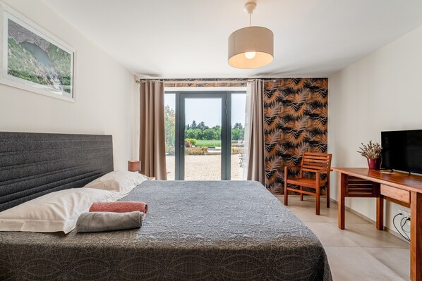 Un dormitorio con cama, escritorio, silla, televisor y vista al exterior.