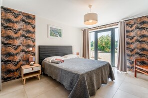 A bedroom with a bed, nightstand, lamp, and a view of the outdoors through a glass door.