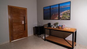 Una habitación con puerta de madera, un escritorio con computadora, una cafetera y un cuadro colgado en la pared.