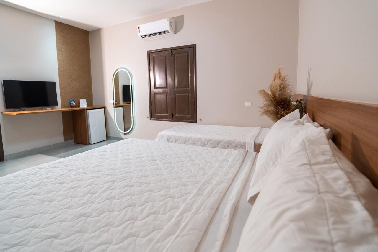 A hotel room with two beds, a TV, a mirror, an air conditioner, and a wooden headboard.