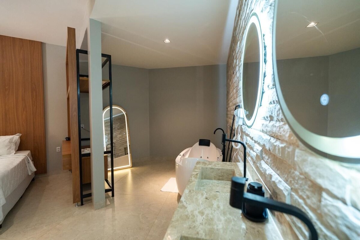 A modern hotel room with a bed, a vanity with a mirror, a shower area, and a wooden wardrobe.