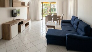 A modern living room with a sectional sofa, a flat-screen TV, a wooden entertainment unit, and a dining area with a table and chairs. - BUNGALOWS SUN CLUB (San Bartolomé de Tirajana)
