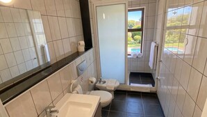 A bathroom with a sink, toilet, and shower area, with a view of a garden through a glass door. - BUNGALOWS SUN CLUB (San Bartolomé de Tirajana)