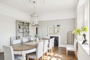 A dining room with a wooden table, white chairs, a chandelier, a fireplace, and a bookshelf. - Rectory & Coach House, Pool, Hot Tub, Padel Courts (Berrynarbor)