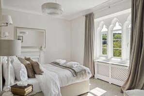A bedroom with a large bed, a chandelier, a mirror, and a window with curtains. - Rectory & Coach House, Pool, Hot Tub, Padel Courts (Berrynarbor)