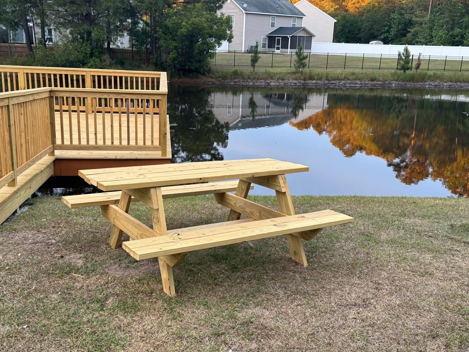 Una mesa de picnic de madera con bancos, una terraza de madera y un estanque al fondo.